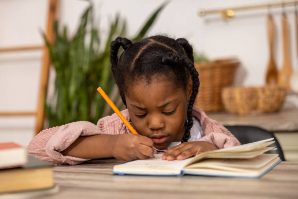 Tired multicultural girl writing in her exercise book with sad expression at home