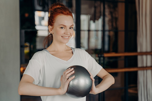 Confident woman in activewear holding a medicine ball, ready for a workout session.