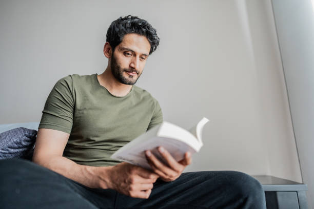 istock Mid adult man reading a book at home 2151158930