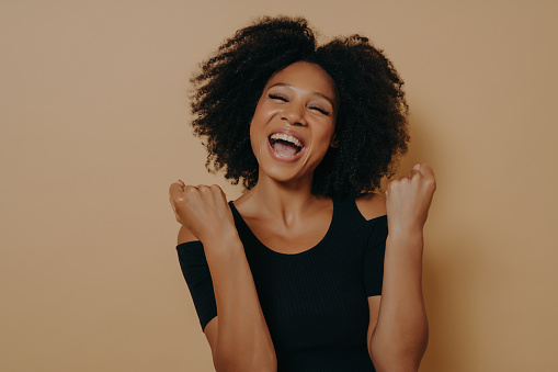 Radiant woman with afro laughing heartily, beige tone setting.