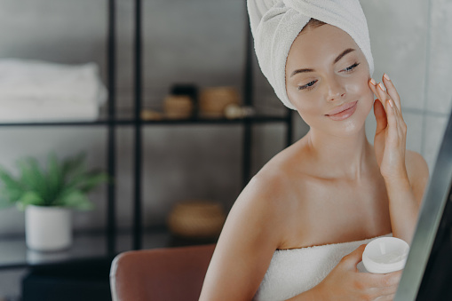 Woman in spa ambiance gently applying facial cream, embodying self-care and relaxation.