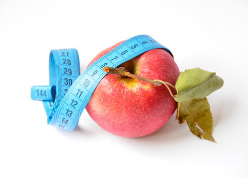 red apple and soft centimeter on a white background. diet and proper nutrition. fight against excess weight. measuring the volume of body parts