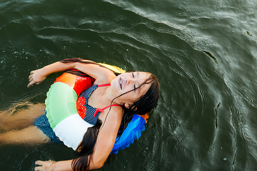 Girl enjoys swimming with inflatable ring in a lake on a hot summer day