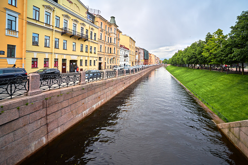 Sankt-Petersburg, Russia - June 03, 2023: Embankment of Admiralty canal with old multicolored residential buildings and green lawn trees near city park \