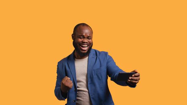 istock Happy man playing videogames on smartphone, celebrating, studio background 2151173491
