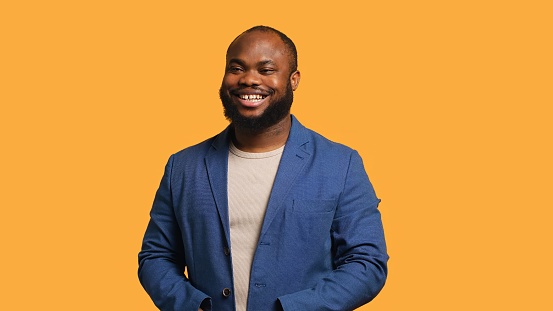 Portrait of joyous african american man holding hands together, smiling, looking pleased, studio background. Upbeat BIPOC person elegantly dressed exulting, feeling satisfied, camera A