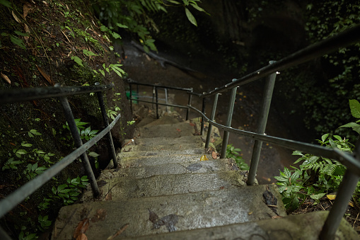 Moss-covered stairs lead to a mountain crevice with a waterfall in the jungle on the popular tourist island of Bali