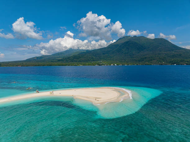 Bali - White sandy Dreamland beach meets the clear blue waters of the ocean, offering a serene view with a distant mountain visible on the horizon under a bright sky.