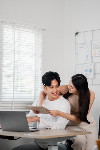 In their light-filled home office, a couple engages in a productive planning session, with the woman leaning over the man as he holds a document.