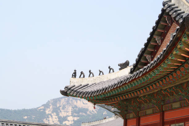 A picture of a rooftop in Gyeongbokgung Palace with dragon statues on the edge. A mountain is in the background.