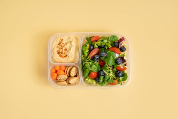 Lunch box with salad and hummus on yellow background