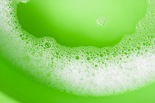 Close-up of soap suds (bubbles foam) with water on a green water background. Space for copy.