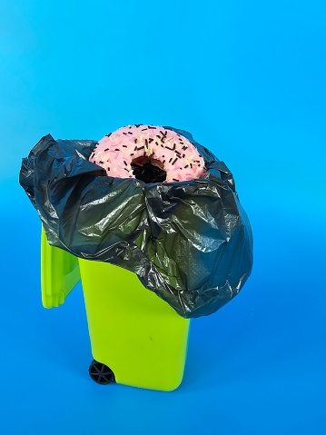 A single donut is seen on top of a metal trash can