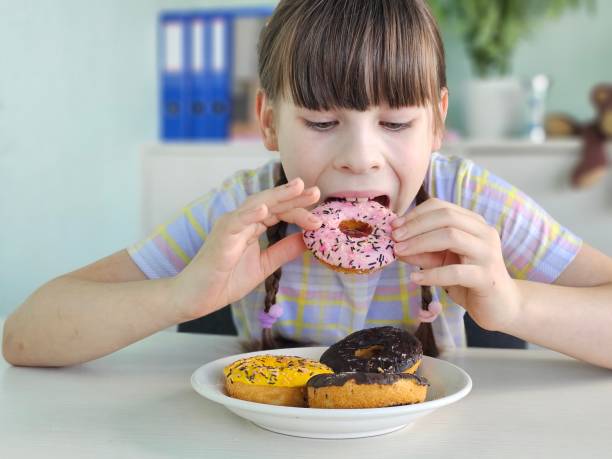 istock A young girl sits at a table and eats a sweet donut 2151216707