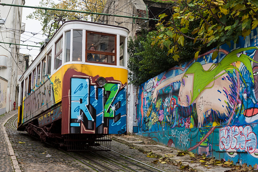Lisbon, Portugal: 10th December, 2019.  One of the two Ascensor da Glória trams covered in graffiti and descending the Calçada da Glória hill from Bairro Alto to Restauradores: a popular tourist attraction.