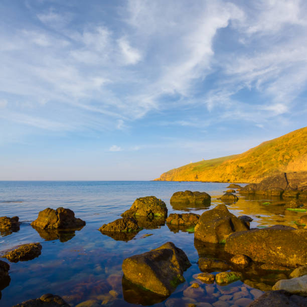 Tranquil Bulgarian seaside landscape with quiet blue reflective Black Sea and old dark rocky stones against bright sunny evening sunset