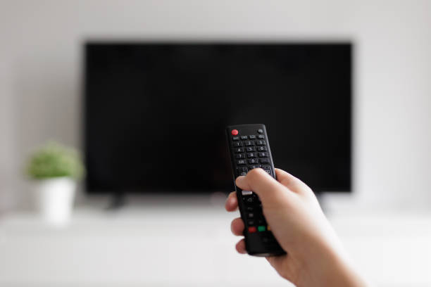istock Close up of hand with remote controller and tv on background 2151220379