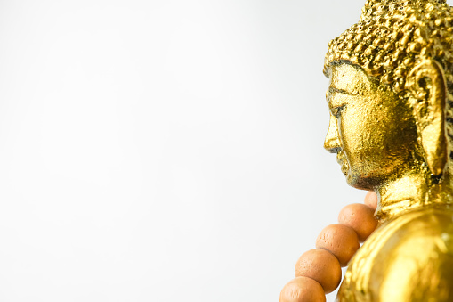 A golden statue of a Buddha figure meditating and wearing prayer beads isolated on white background. Concept for Vesak Day and Enlightenment Day