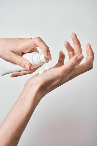Two female hands, one of which applies moisturizer to the other hand.