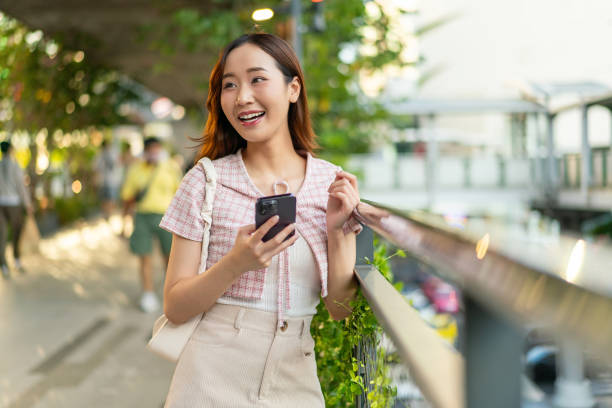 istock Sunlit Connection: Young Asian Woman with Smart Phone on Footpath 2151228853