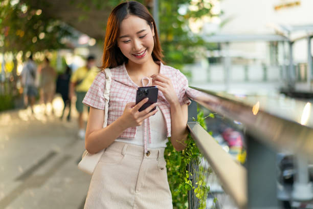 istock Sunlit Connection: Young Asian Woman Uses Phone on Footpath 2151228874