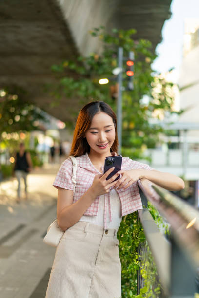 istock Sunlit Connection: Young Asian Woman Uses Phone on Footpath 2151229000
