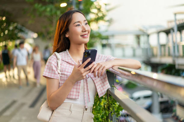 istock Sunlit Connection: Young Asian Woman with Smart Phone on Footpath 2151229003