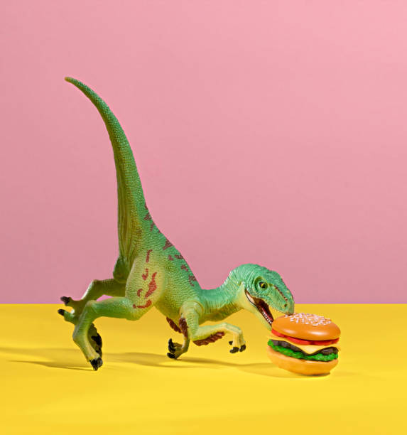 istock Green dinosaur bites a burger on pink and yellow background. 2151229463