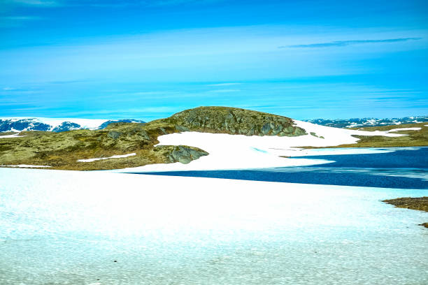Snowcapped mountains hill and land next to blue lake in Norway