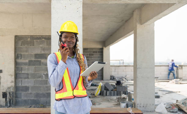 istock A builder in safety uniform standing at a building site, holding a walkie-talkie communicating with other team member. Tablet in her hand used for reviewing construction plan or checking schedule. 2151234937