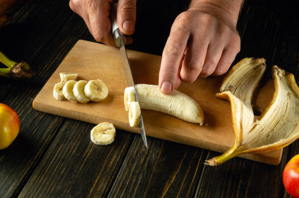 istock Finely sliced banana on a kitchen wooden board. Cooking a fruit dish on the kitchen table with the hands of a chef. Place for advertising 2151235640