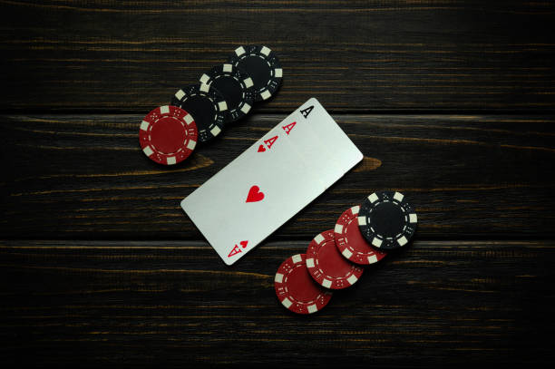 istock Black and red chips and playing cards with a winning combination of three kind or set on a black vintage table. Concept of winning in a poker club or casino with three aces 2151235760