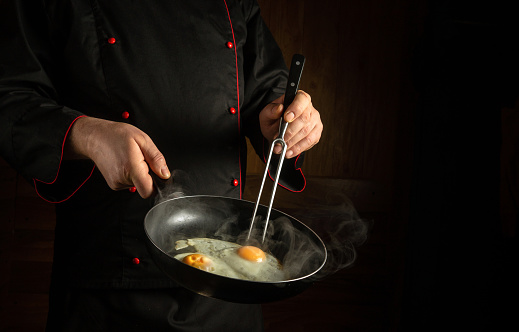 Cooking scrambled eggs in a frying pan. The chef holds a fork and a frying pan with a fried egg. Dark space for advertising.