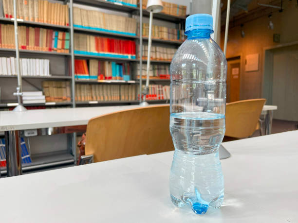 istock Half-Full Plastic Water Bottle on a Library Table With Bookshelves in the Background 2151237017