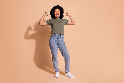 Full length photo of perky confident woman wear khaki t-shirt jeans trousers indicating at herself isolated on beige color background.
