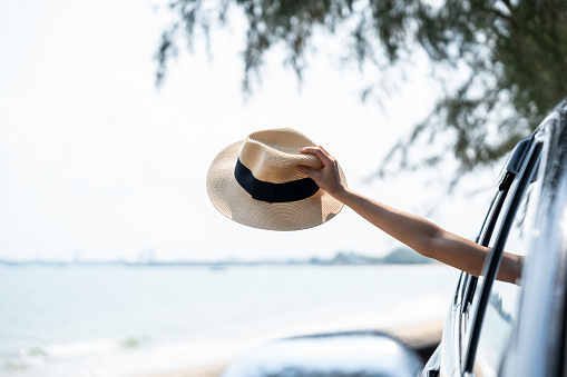 Young woman drove to the provinces sea sand beach. Parked on the side of the road raised hand holding hat from the car window. Safety travel by car vehicle