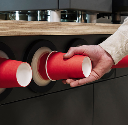 Close-up of a hand pulling a red paper cup from a modern cup dispenser in a cafeteria setting
