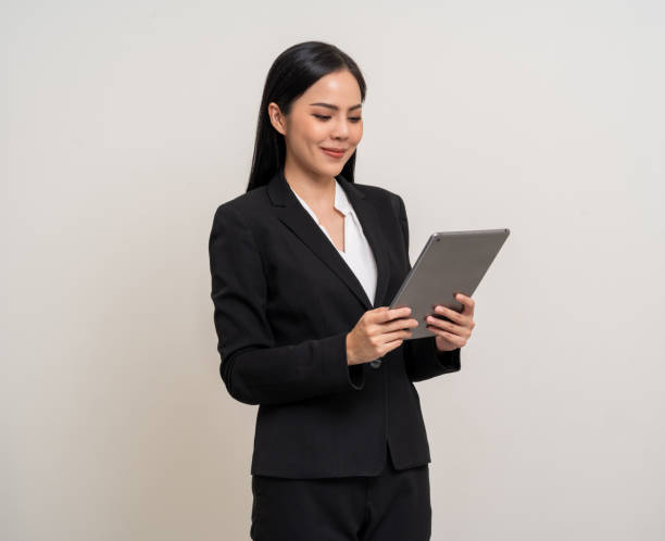 istock Attractive elegant young asian business woman using digital tablet standing on isolated background. Happy young latin female formal black suit holding tablet gadget working service with customer 2151241411