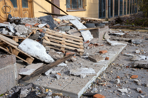 A pile of construction waste in front of a building undergoing reconstruction: wooden pallets, pieces of broken concrete floors and walls, old tires and dusty debris. Repair and construction concept