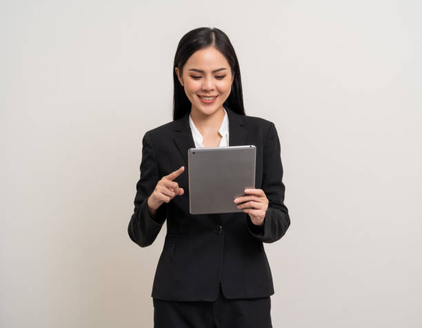istock Attractive elegant young asian business woman using digital tablet standing on isolated background. Happy young latin female formal black suit holding tablet gadget working service with customer 2151242179