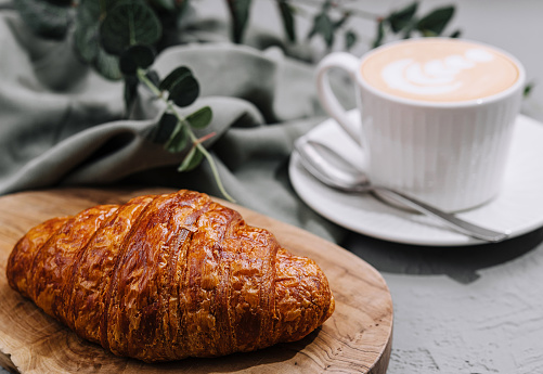 Delicious golden croissant paired with a creamy latte, presented on a wooden board
