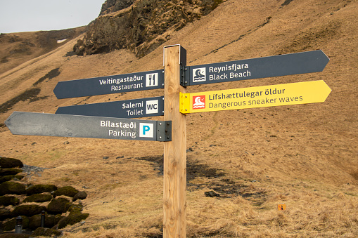Vik, Iceland - march 13th, 2023: Wooden signpost with directions arrows to attractions on black sand beach in Reynisfjara . Iceland navigation and information signs