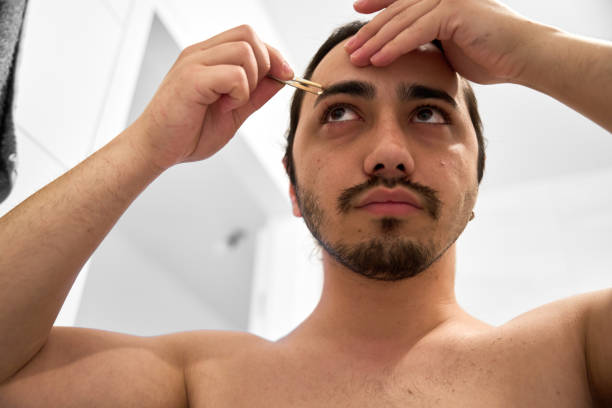 istock young man is plucking his eyebrows with tweezers 2151250326