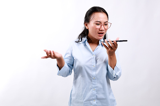 Angry asian business woman asking and shouting at mobile phone, looks outraged, furious while talking on smartphone, standing over white background