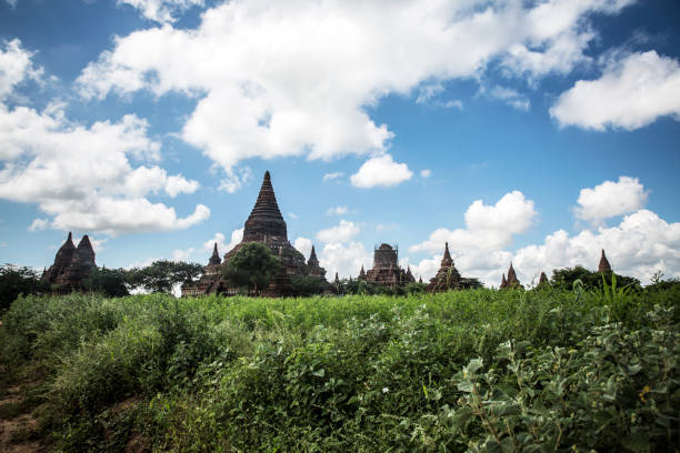 Bagan, Myanmar - October 15, 2017:In Bagan, green grasslands stretch under a sky of blue and white clouds. Numerous pagodas dot the horizon.