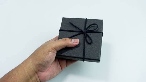 istock Black gift box with texture with black ribbon isolated on white background. Black box being held in hand 2151255027