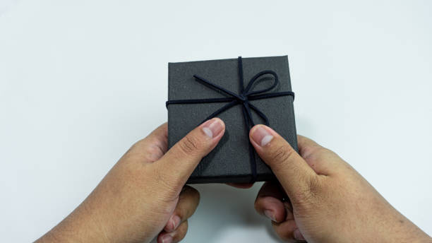 istock Black gift box with texture with black ribbon isolated on white background. Black box being held in hand 2151255047