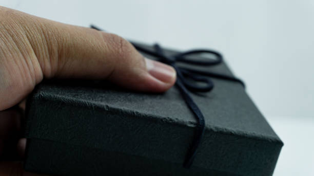 istock Black gift box with texture with black ribbon isolated on white background. Black box being held in hand 2151255627