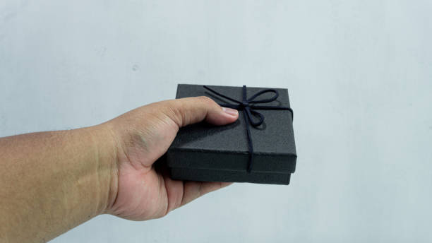 istock Black gift box with texture with black ribbon isolated on white background. Black box being held in hand 2151255673