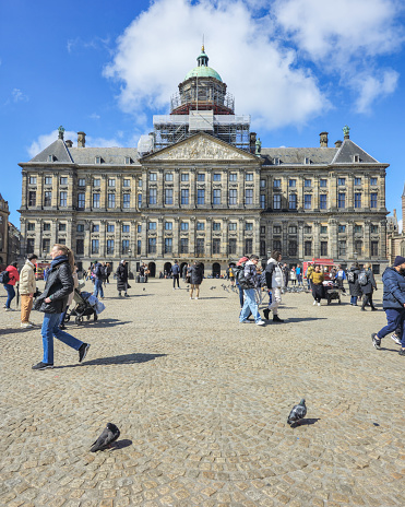 Amsterdam Netherlands 21 April 2024, A diverse group of people exploring the grand architecture building, admiring its intricate details and chatting animatedly as they stroll around Dam square